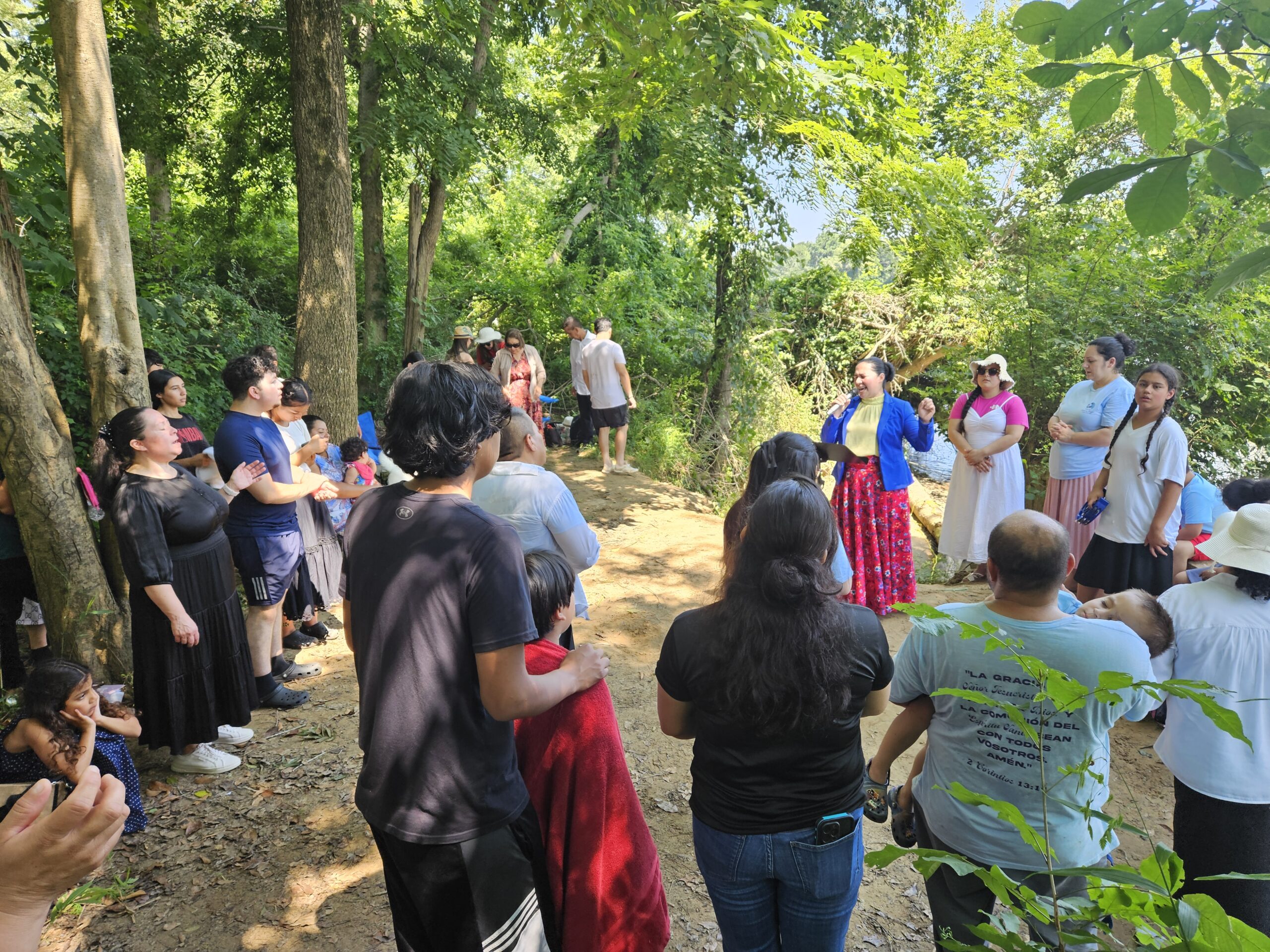 Congregación de la Iglesia Cristiana Pacto de Gracia en Charlotte reunida en un bosque para celebrar bautizos, con hermanos y hermanas participando en oración y adoración en un ambiente natural.