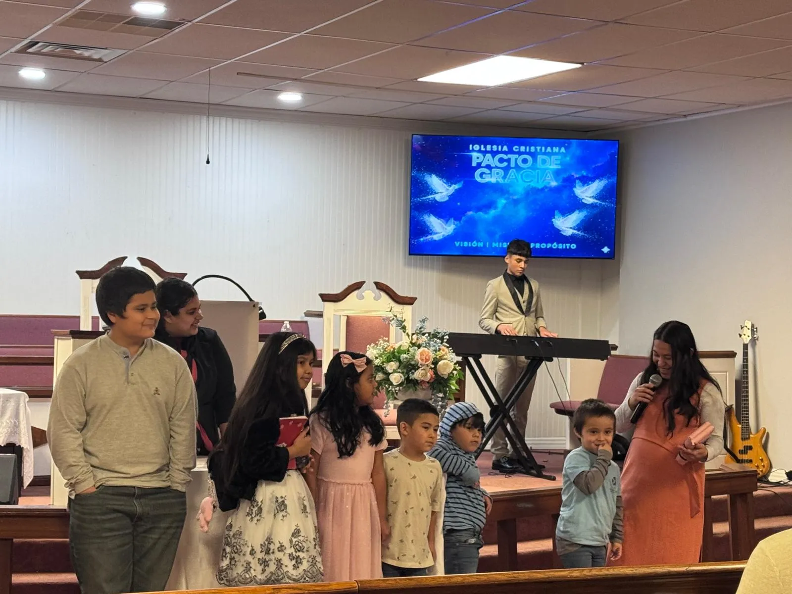 Niños y jóvenes de la Iglesia Cristiana Pacto de Gracia en Charlotte participando en un culto especial, acompañados por adultos y música congregacional, unidos en alabanza y adoración.