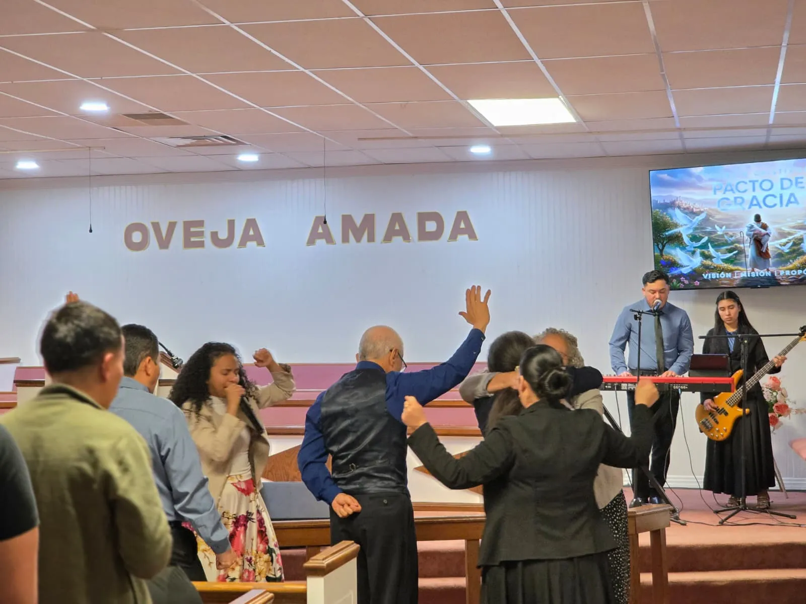 Congregación de la Iglesia Cristiana Pacto de Gracia en Charlotte participando en un servicio especial con músicos y predicación, bajo el mensaje “Gloria a Dios” en el altar.