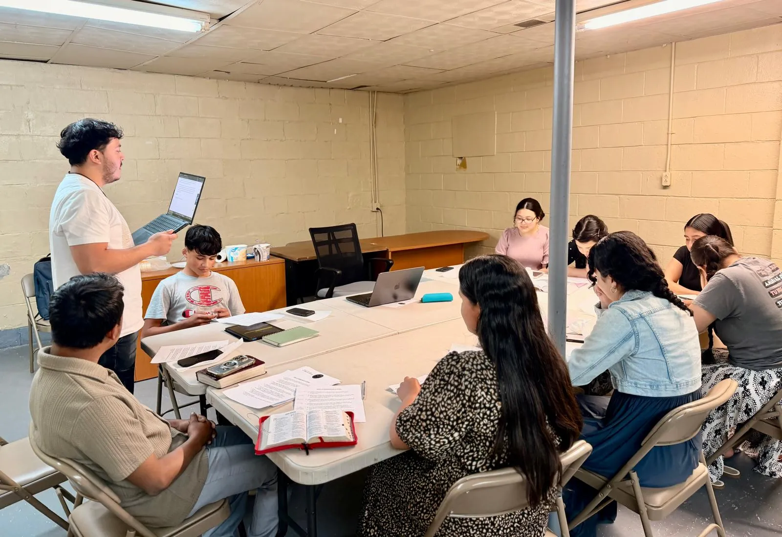 Jóvenes de la Iglesia Cristiana Pacto de Gracia en Charlotte participando en un taller de formación y discipulado, reunidos en mesa con materiales de estudio y dirigidos por un líder.