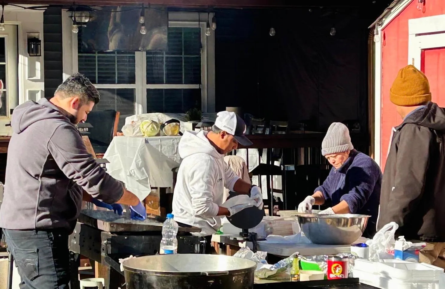 Miembros de la Iglesia Cristiana Pacto de Gracia en Charlotte preparando alimentos al aire libre para apoyar las misiones, trabajando en equipo con mesas llenas de utensilios y recipientes.