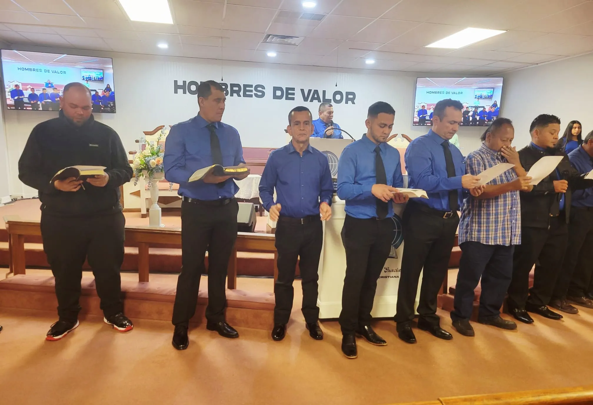 Caballeros de la Iglesia Cristiana Pacto de Gracia en Charlotte participando en un servicio especial, vestidos formalmente y sosteniendo certificados frente al altar con el mensaje “Palabra de Vida